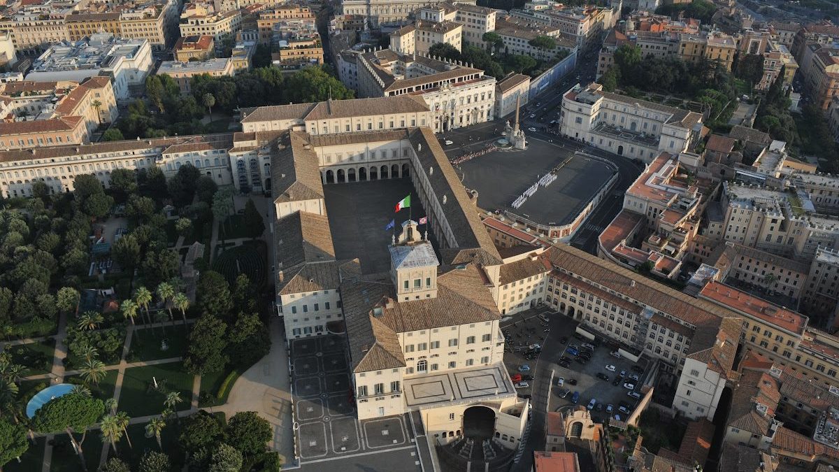 Vista aérea da Colina Quirinal, destacando o imponente Palácio do Quirinal, residência oficial do Presidente da Itália, cercado por jardins luxuriantes e a arquitetura histórica de Roma ao fundo.